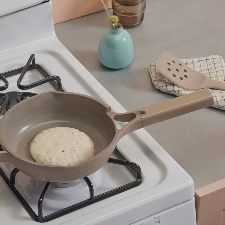 flipping pancake on stove with beige slotted turner