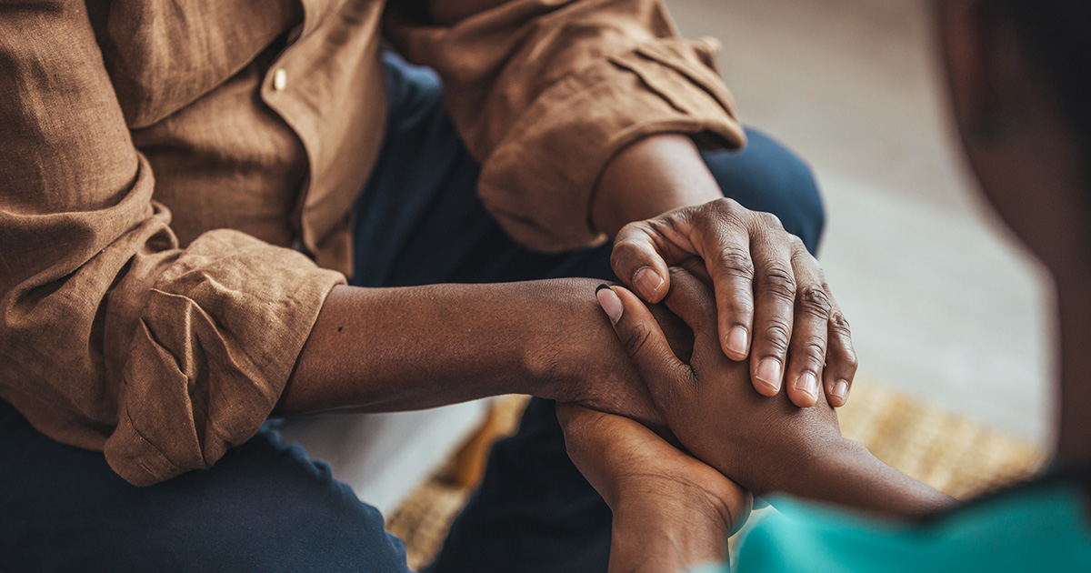 Two people sit facing each other, holding hands.