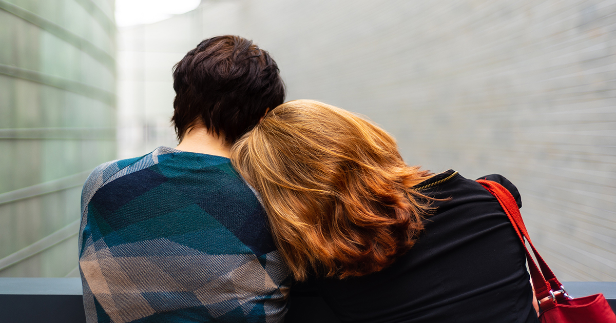 A woman rests her head on a friend’s shoulder.