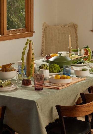 A dining table decorated with white dinnerware, colorful drinking glasses, food, and candles