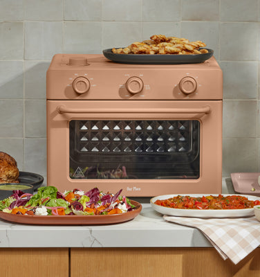 pink large wonder oven on counter surrounded by an assortment of cooked food