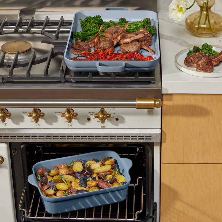 cooking lamb chops, broccoli, and peppers on blue griddle pan on stove. baking potatoes on blue baker in oven