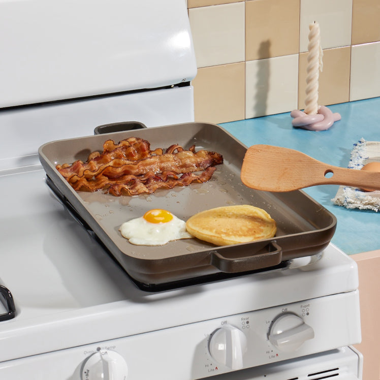 cooking bacon, eggs and pancakes on black griddle pan on stove