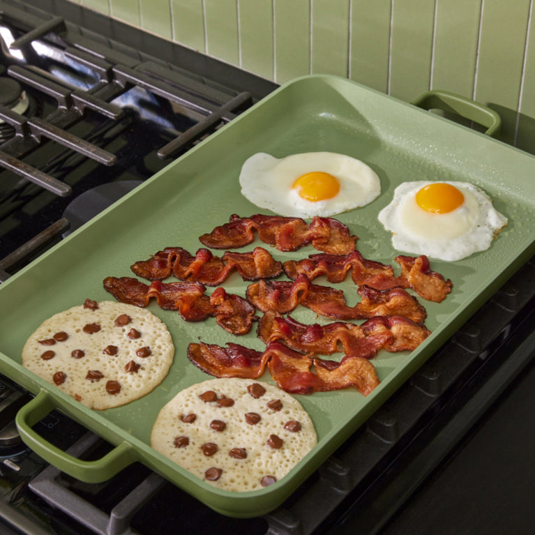 cooking eggs, back and pancakes on green griddle pan on stove