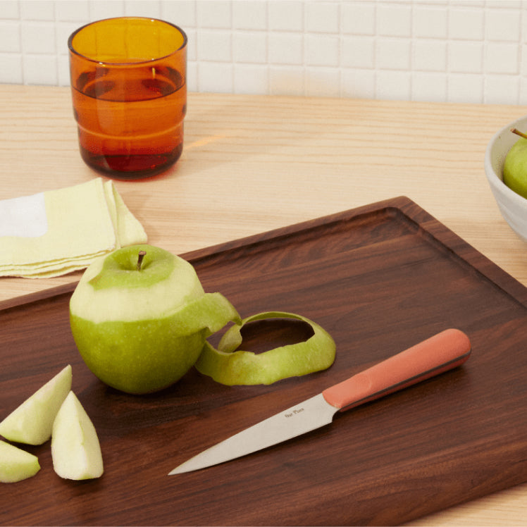 Pink Precise Paring Knife on top of the Walnut Cutting Board with a peeled apple