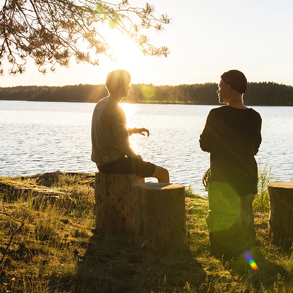 Two men sitting on tree stumps by a lake at sunset.
